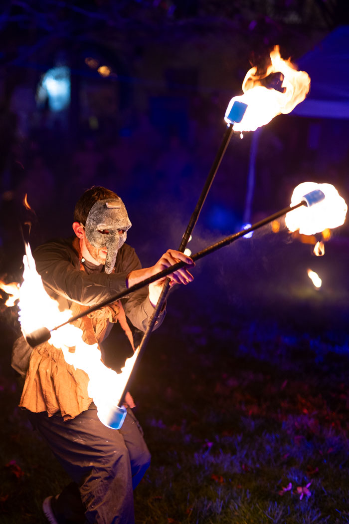 A man performing at a fire show with a mask on and fire sticks in his hands.