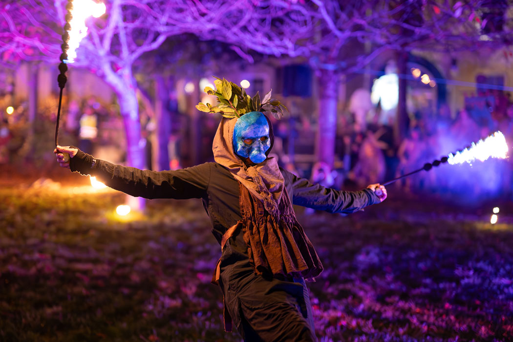 A man performing at a fire show with a mask on and fire sticks in his hands.